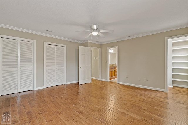 unfurnished bedroom with visible vents, baseboards, two closets, ornamental molding, and light wood finished floors