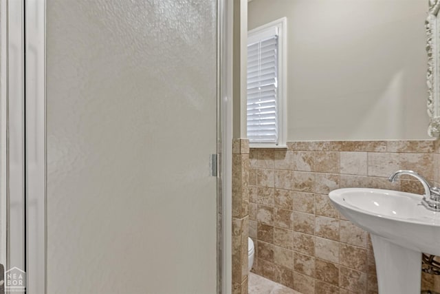 full bath featuring a stall shower, toilet, wainscoting, tile walls, and a sink