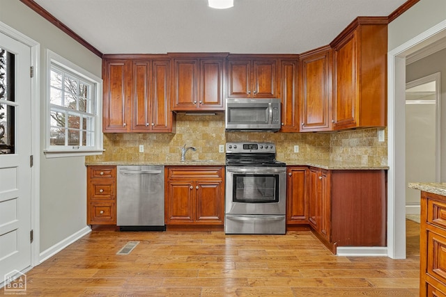 kitchen featuring a sink, ornamental molding, light wood-type flooring, light stone countertops, and stainless steel appliances