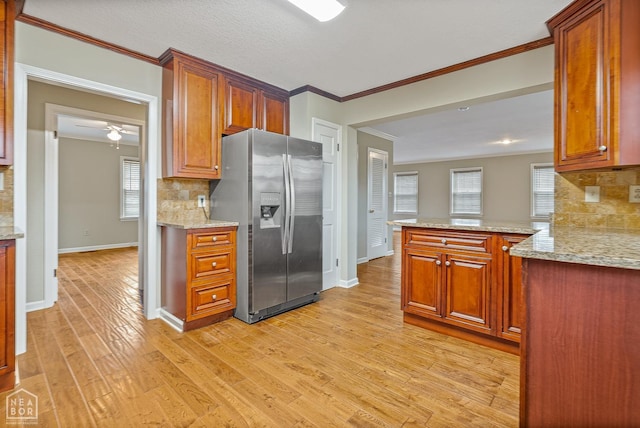 kitchen with stainless steel fridge, crown molding, brown cabinetry, light wood finished floors, and light stone countertops