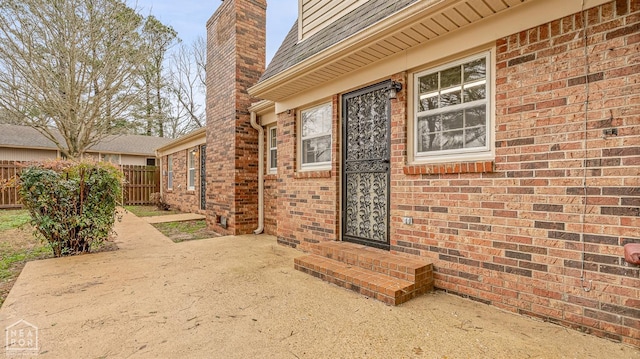 doorway to property featuring a patio, a chimney, fence, and brick siding