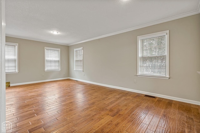 spare room featuring light wood-style floors, visible vents, baseboards, and crown molding