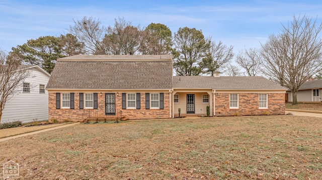 view of front of property featuring roof with shingles, a front yard, and brick siding