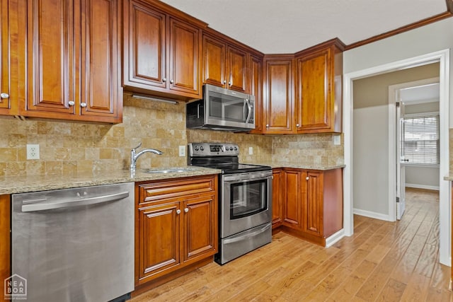 kitchen with tasteful backsplash, a sink, light wood-type flooring, light stone countertops, and stainless steel appliances
