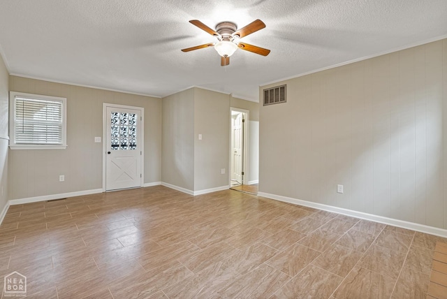 empty room with crown molding, a textured ceiling, a ceiling fan, visible vents, and baseboards