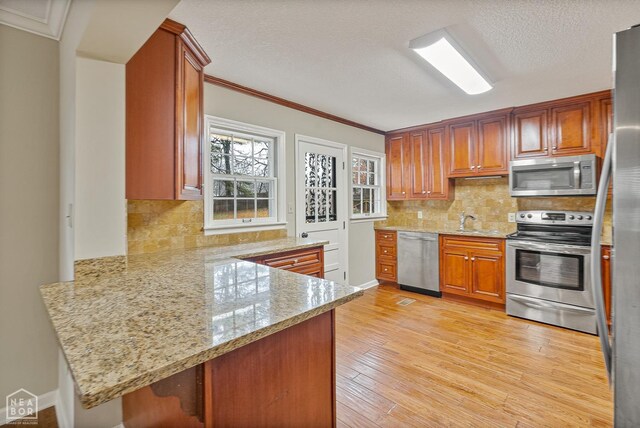 kitchen featuring ornamental molding, a peninsula, light wood-style flooring, backsplash, and stainless steel appliances