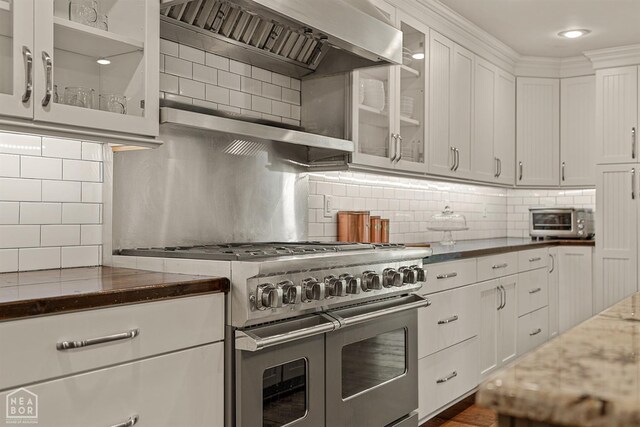 803 Fairway Dr, Jonesboro, AR 72401 - kitchen with wall chimney range hood, range with two ovens, white cabinetry, and decorative backsplash