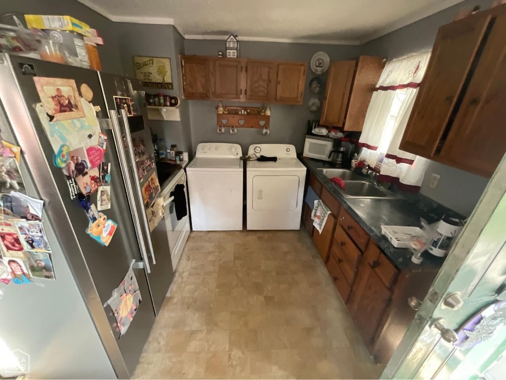 kitchen with white microwave, freestanding refrigerator, a sink, brown cabinets, and washing machine and dryer