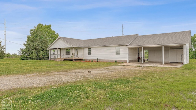 ranch-style home featuring a front lawn, dirt driveway, an attached carport, and a shingled roof