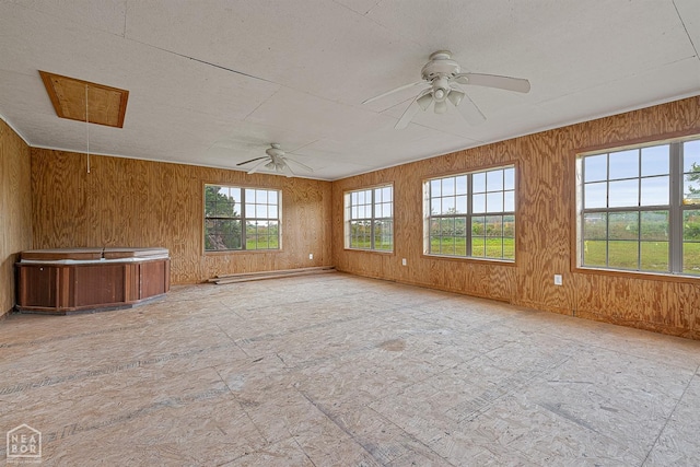unfurnished room featuring attic access, a ceiling fan, wooden walls, and baseboards
