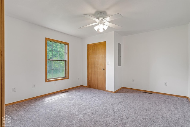 spare room with electric panel, a ceiling fan, visible vents, carpet, and baseboards