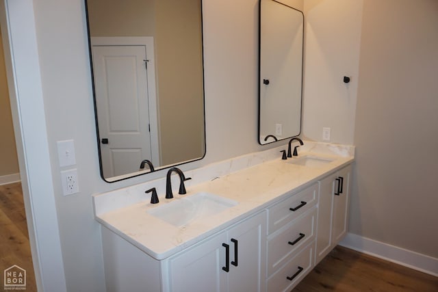full bath with baseboards, double vanity, a sink, and wood finished floors