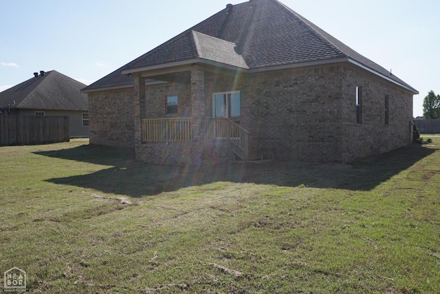 view of side of home featuring a yard, fence, a shingled roof, and brick siding