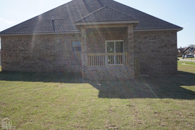 rear view of house with a lawn, roof with shingles, and brick siding