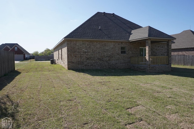 back of property featuring brick siding, roof with shingles, fence, and a lawn