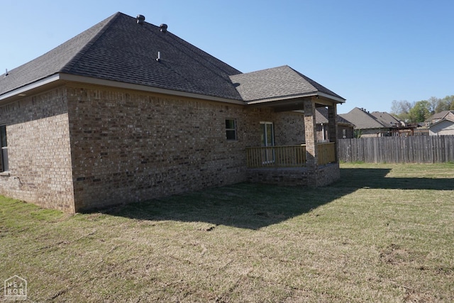 back of property featuring roof with shingles, fence, brick siding, and a lawn