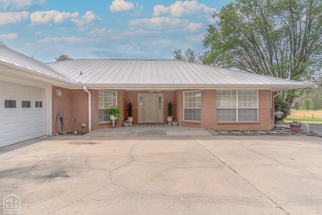 single story home with concrete driveway, brick siding, an attached garage, and metal roof