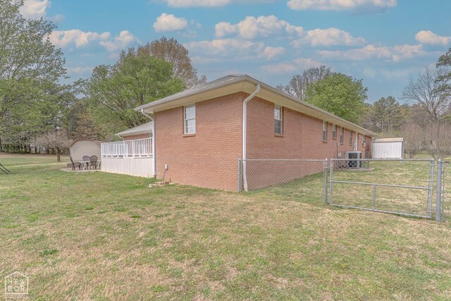 view of property exterior featuring an outdoor structure, a shed, brick siding, a yard, and fence