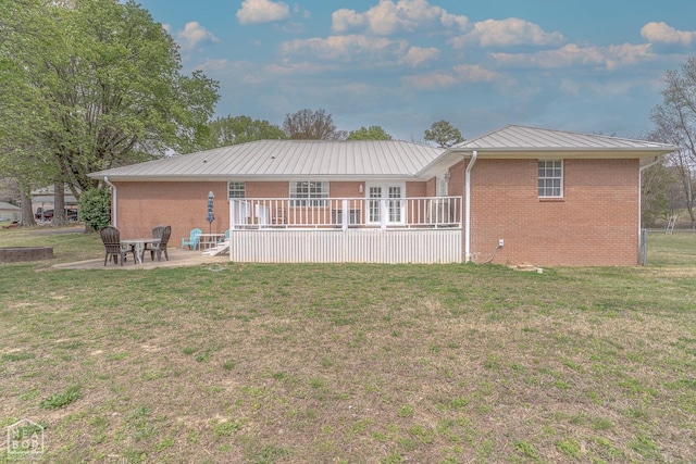 rear view of house with a patio, a lawn, metal roof, and brick siding