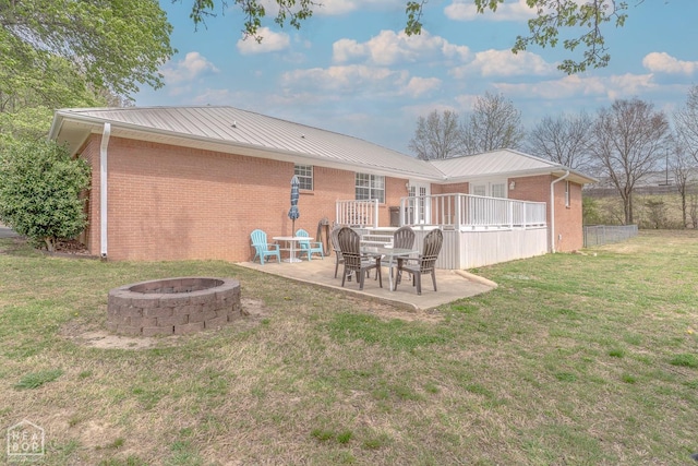 rear view of property featuring a patio area, brick siding, an outdoor fire pit, metal roof, and a lawn