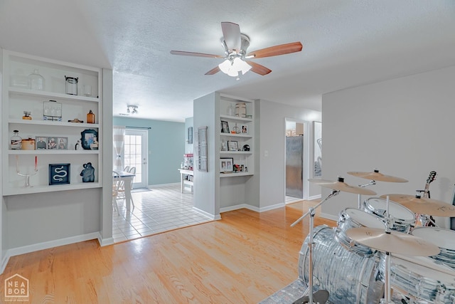 living room with baseboards, built in shelves, a textured ceiling, ceiling fan, and light wood finished floors
