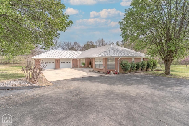 ranch-style house with metal roof, a garage, and driveway