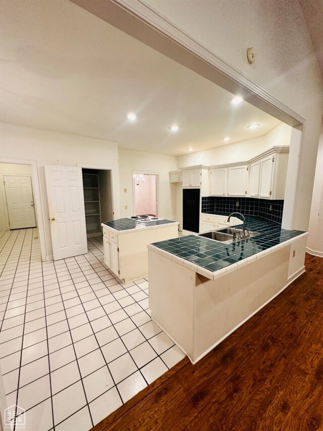 2208 John Cir, Newport, AR 72112 - kitchen with tile countertops, tasteful backsplash, a peninsula, white cabinetry, and a sink