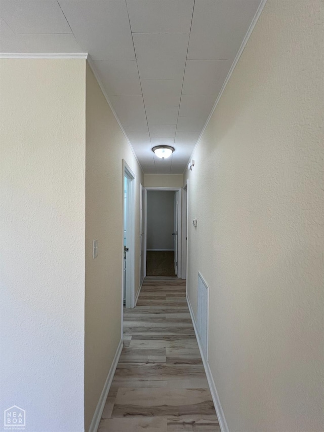 hall featuring ornamental molding, baseboards, light wood finished floors, and visible vents