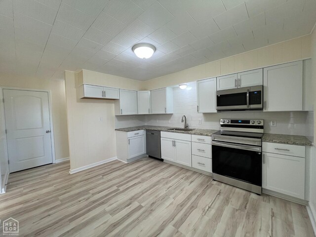 kitchen with light wood-style flooring, light stone counters, a sink, stainless steel appliances, and baseboards