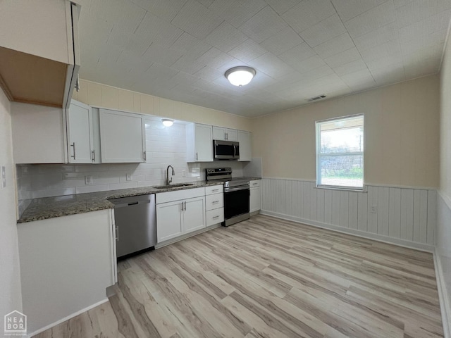 kitchen featuring stainless steel appliances, light wood-style floors, a sink, and dark stone countertops