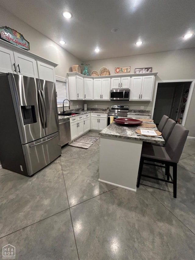 kitchen featuring stainless steel appliances, a sink, a kitchen island, light stone countertops, and white cabinets