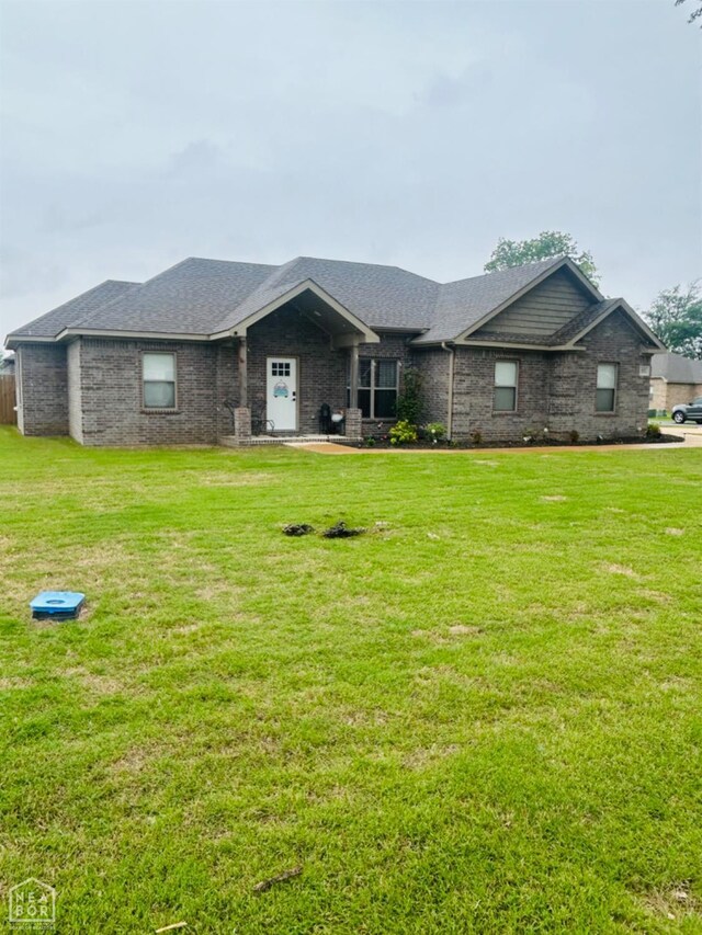 view of front of property with a front lawn, a shingled roof, and brick siding