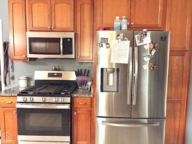 kitchen with dark stone counters, appliances with stainless steel finishes, and brown cabinetry