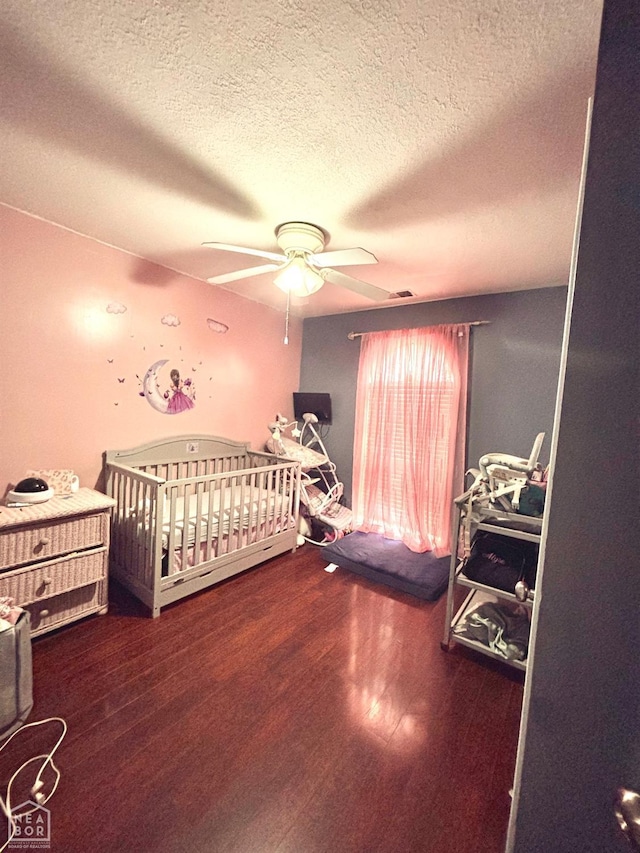bedroom with a ceiling fan, a textured ceiling, wood finished floors, and a crib