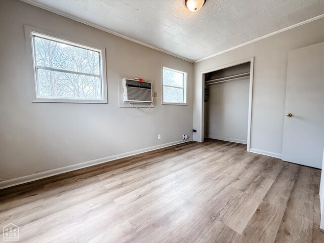 unfurnished bedroom with a closet, an AC wall unit, baseboards, crown molding, and wood finished floors