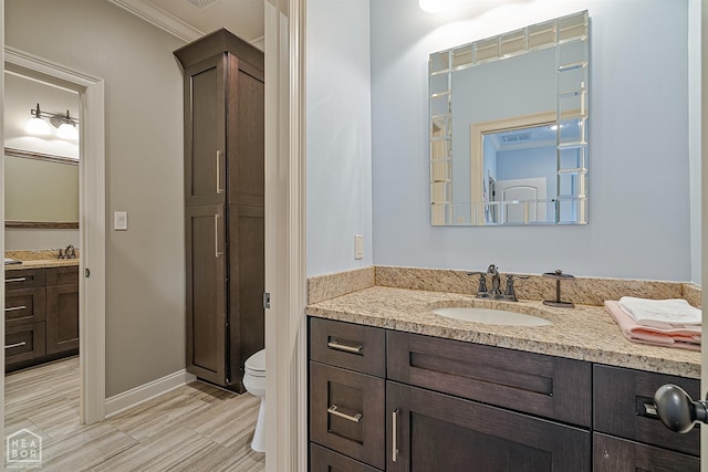 bathroom with toilet, baseboards, vanity, and ornamental molding