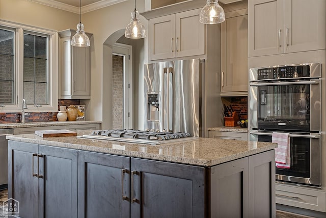 kitchen featuring a sink, crown molding, a kitchen island, arched walkways, and stainless steel appliances