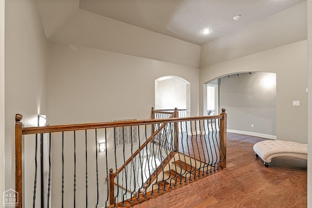 hallway with wood finished floors, an upstairs landing, baseboards, and arched walkways