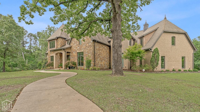 english style home with a chimney, brick siding, stone siding, roof with shingles, and a front lawn