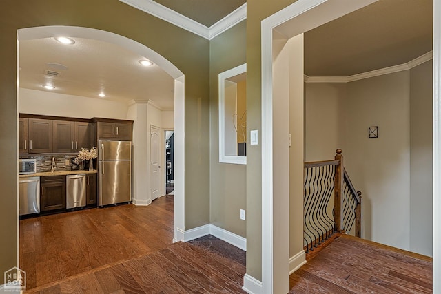 kitchen with dark brown cabinetry, dark wood-type flooring, arched walkways, light countertops, and appliances with stainless steel finishes