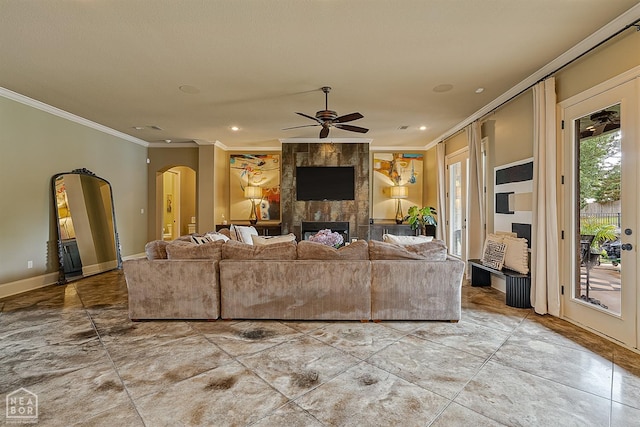living room featuring a fireplace, crown molding, arched walkways, a ceiling fan, and baseboards