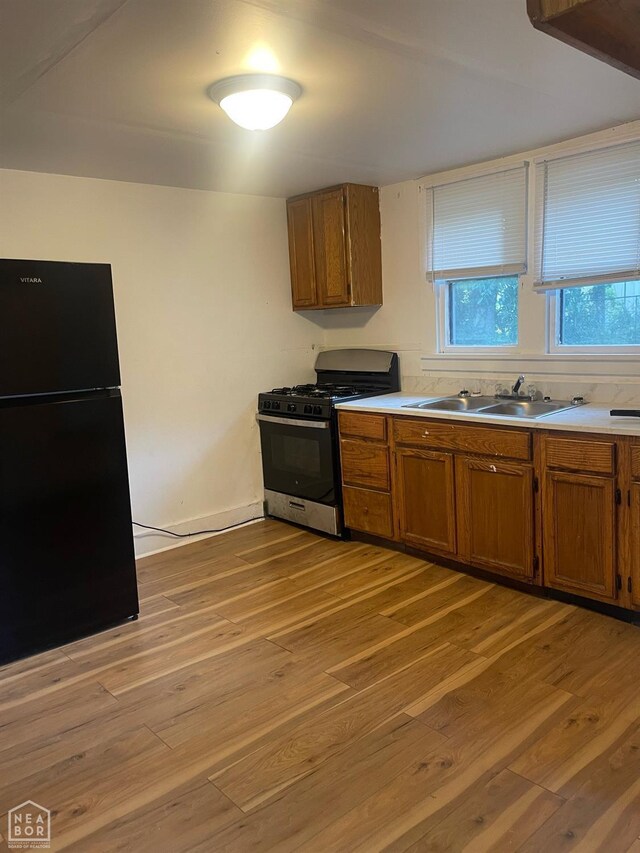 1007 Warren St, Jonesboro, AR 72401 - kitchen featuring freestanding refrigerator, brown cabinetry, light wood-type flooring, gas range, and a sink