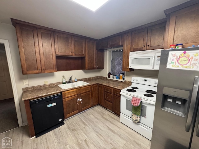 kitchen with a sink, dark countertops, white appliances, and light wood-style floors