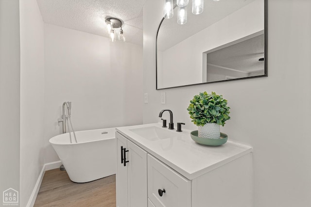 full bathroom featuring wood finished floors, vanity, a textured ceiling, a freestanding bath, and baseboards
