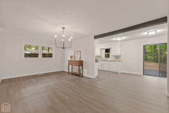 unfurnished living room with light wood-style flooring, a textured ceiling, baseboards, a sink, and a chandelier
