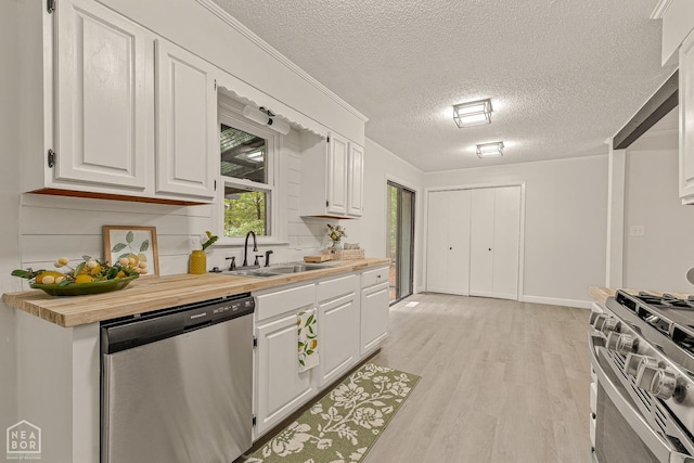 kitchen with a sink, butcher block countertops, light wood finished floors, white cabinets, and appliances with stainless steel finishes