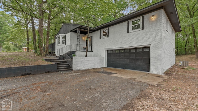 view of front of home with a garage, cooling unit, brick siding, and driveway