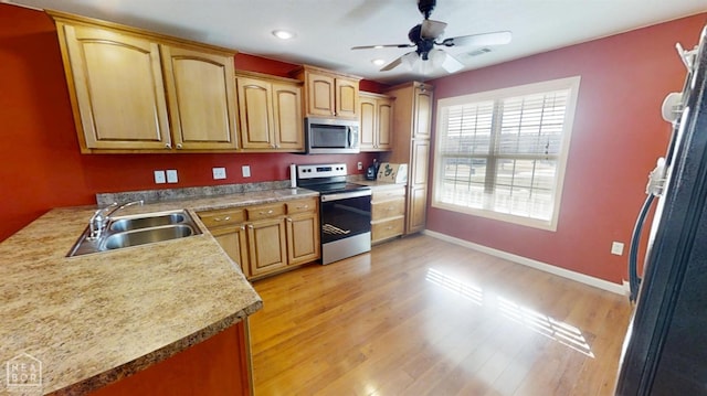 kitchen with baseboards, a sink, ceiling fan, light wood-type flooring, and stainless steel appliances