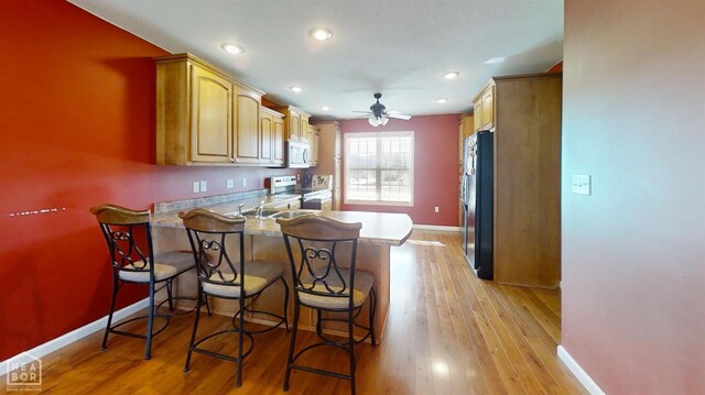 kitchen with white microwave, freestanding refrigerator, ceiling fan, a peninsula, and stainless steel range with electric stovetop