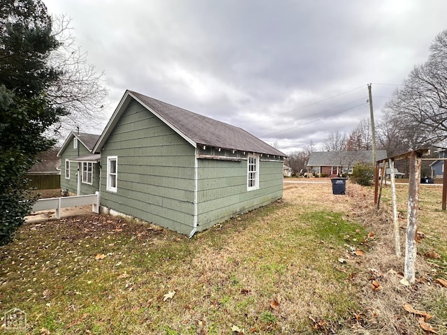 view of side of property with roof with shingles and a lawn